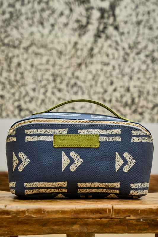 Blue Zola toiletry bag in mudcloth print, with a green leather handle.