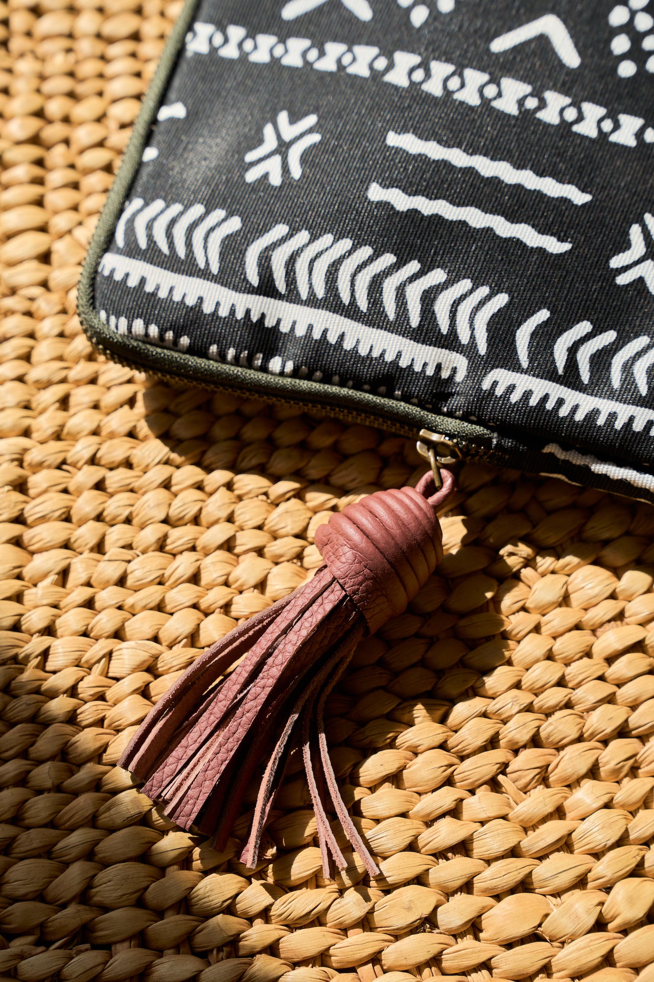 Black mudcloth laptop sleeve with white pattern and pink tassel on a woven surface