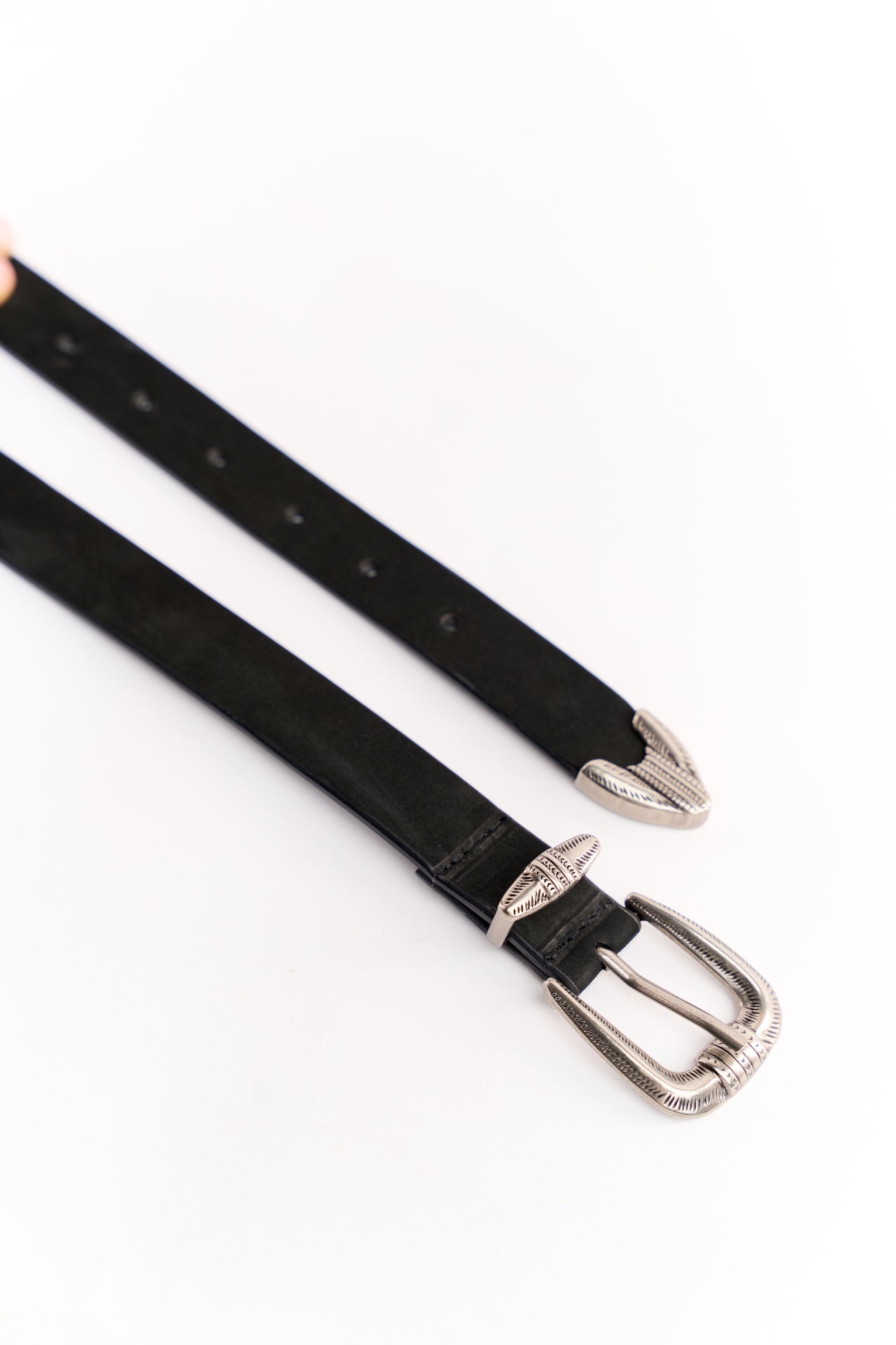 Close-up view of a handcrafted black suede leather belt for women, featuring an ornate silver buckle with intricate engravings and matching pointed silver tips on both ends.