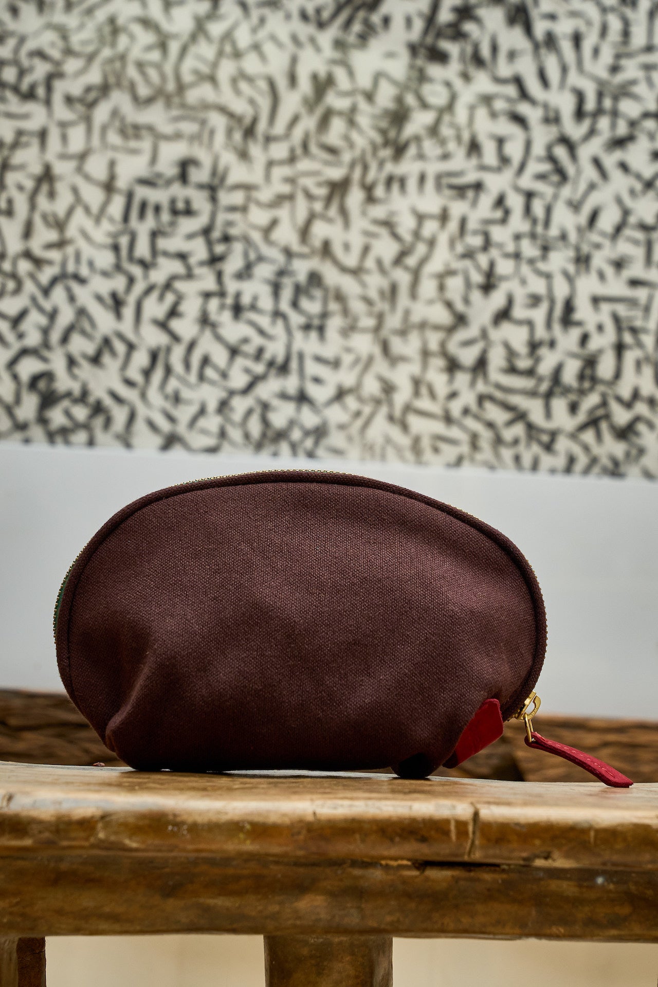 Brown pouch with a red zipper on a wooden surface with a textured wall background