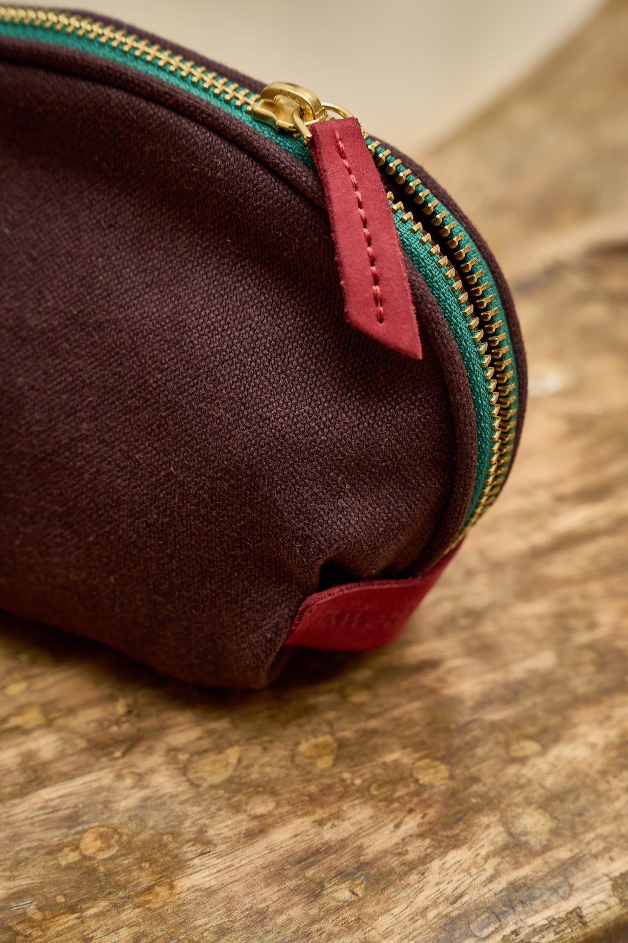 Brown waridi pouch with a red zipper on a wooden surface