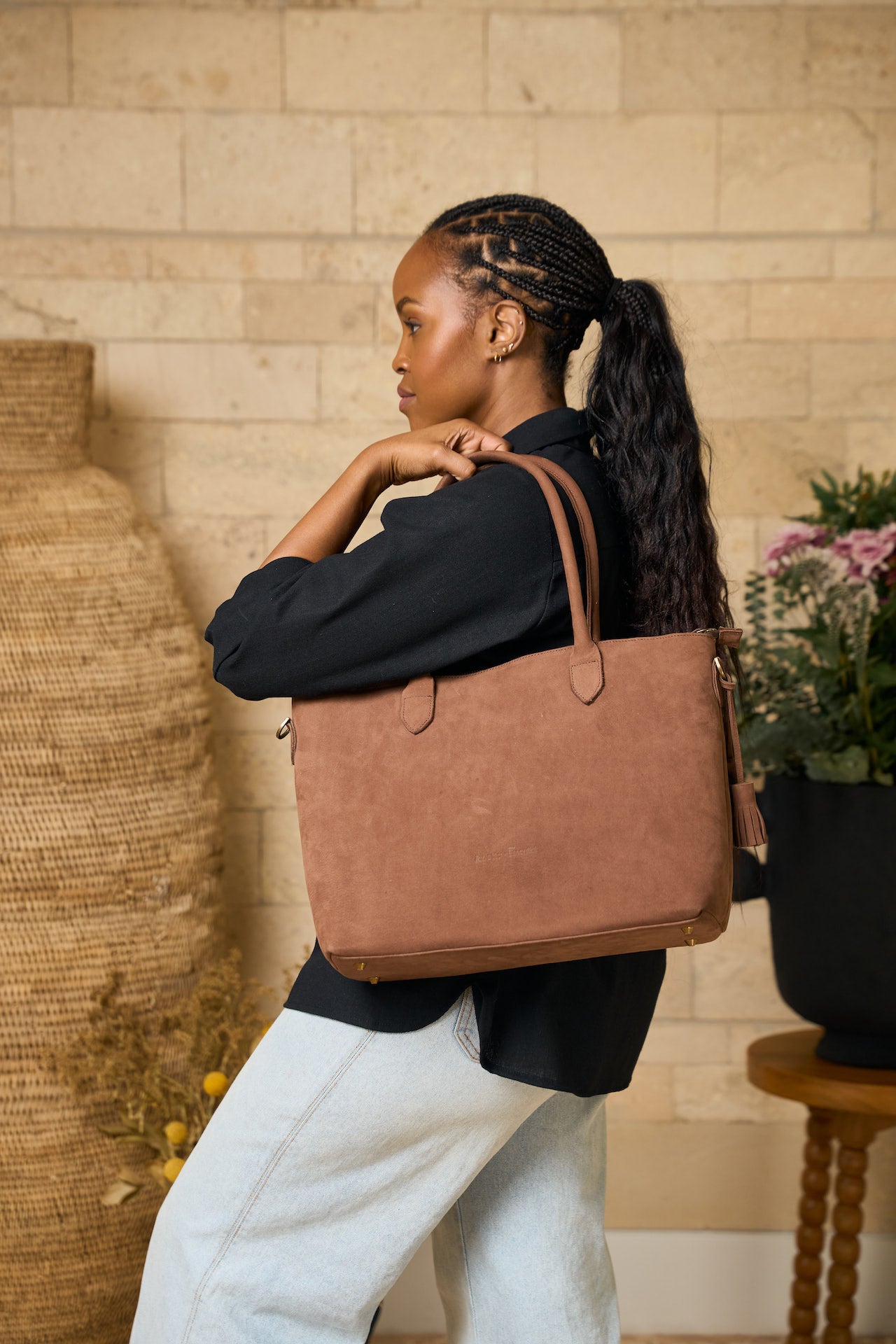Woman carrying a brown leather tote bag in a home setting.