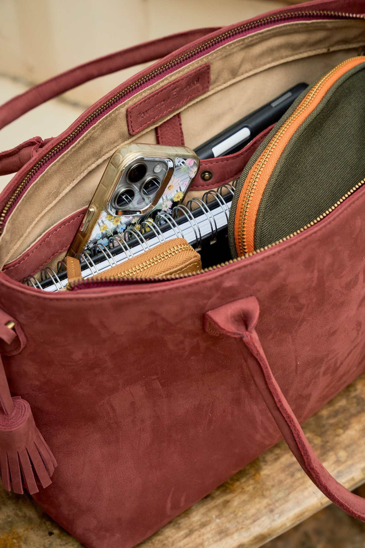 Red suede leather hand  bag with open zipper showing the contents inside 