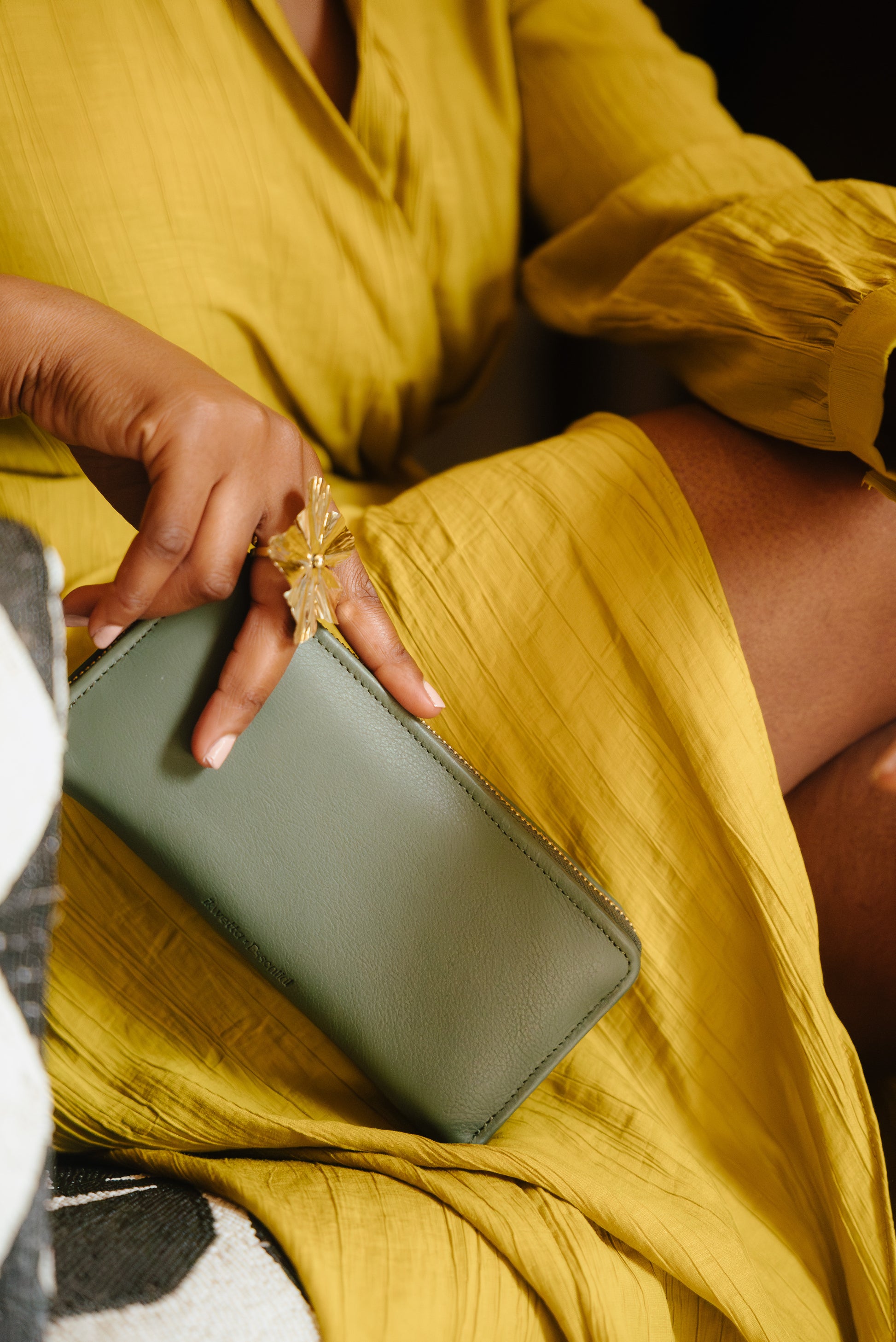 A person holding a green Essential Zip Wallet, which is placed on their lap.