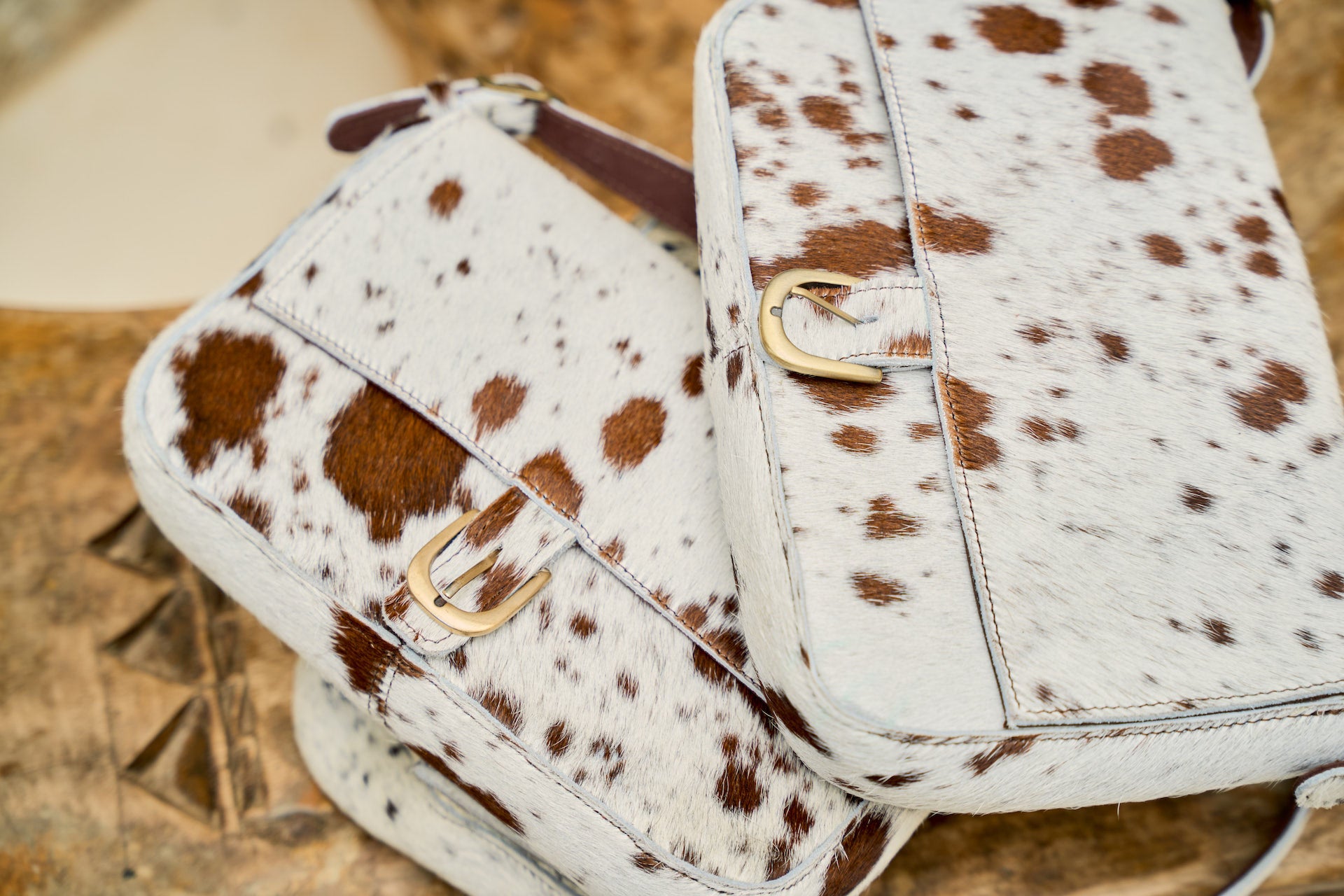 Cow print handbag with gold buckle on a textured surface