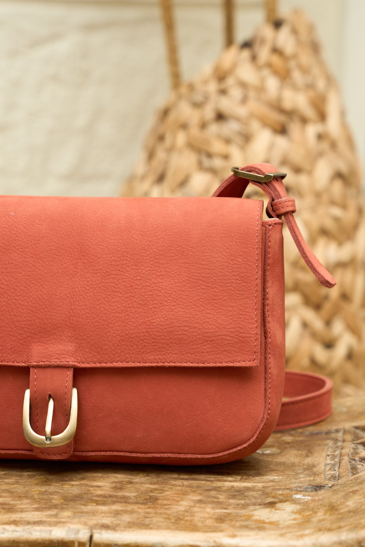 Firebrick suede leather handbag with a gold buckle on a wooden surface.