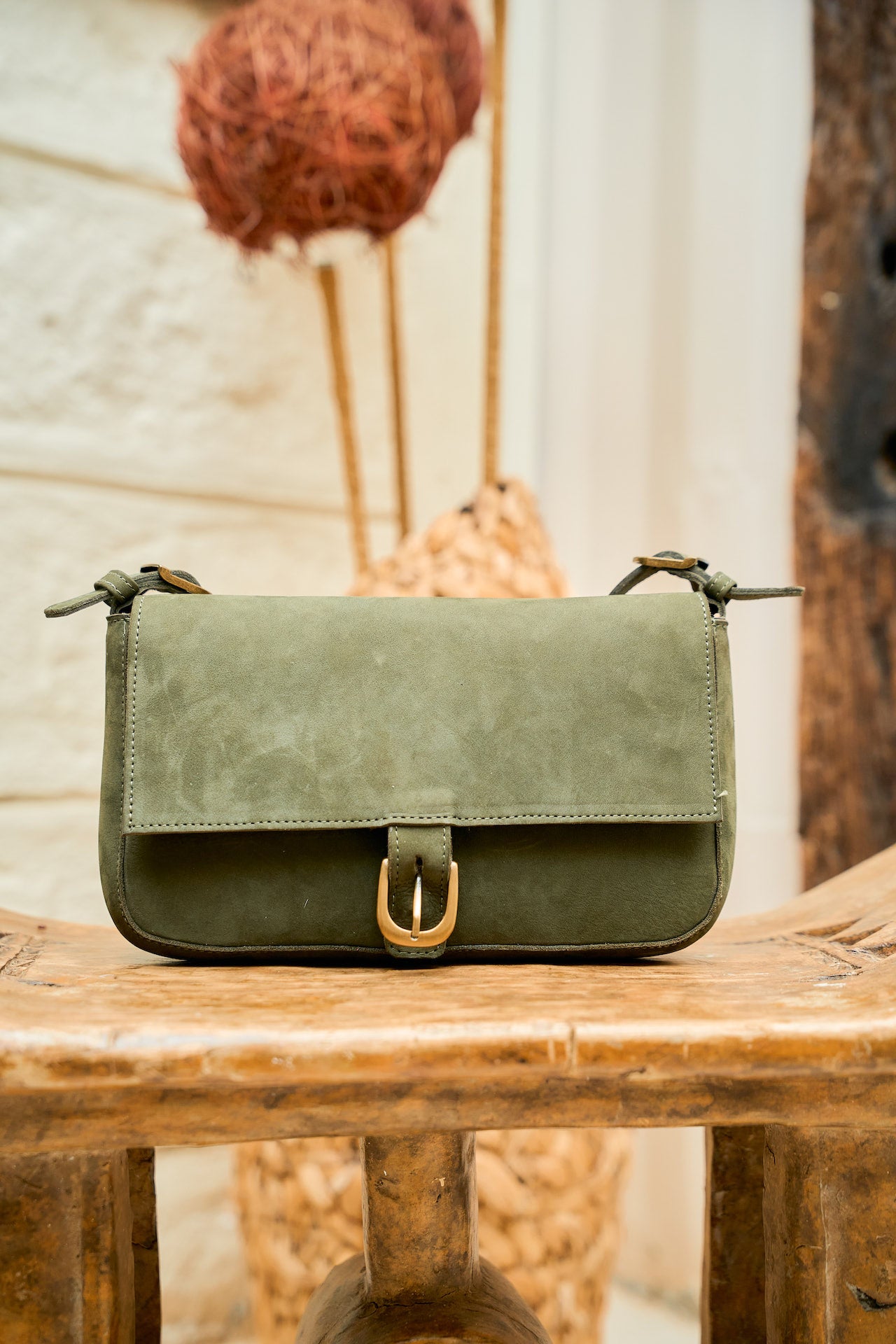 Green leather handbag on a wooden surface with a blurred natural background