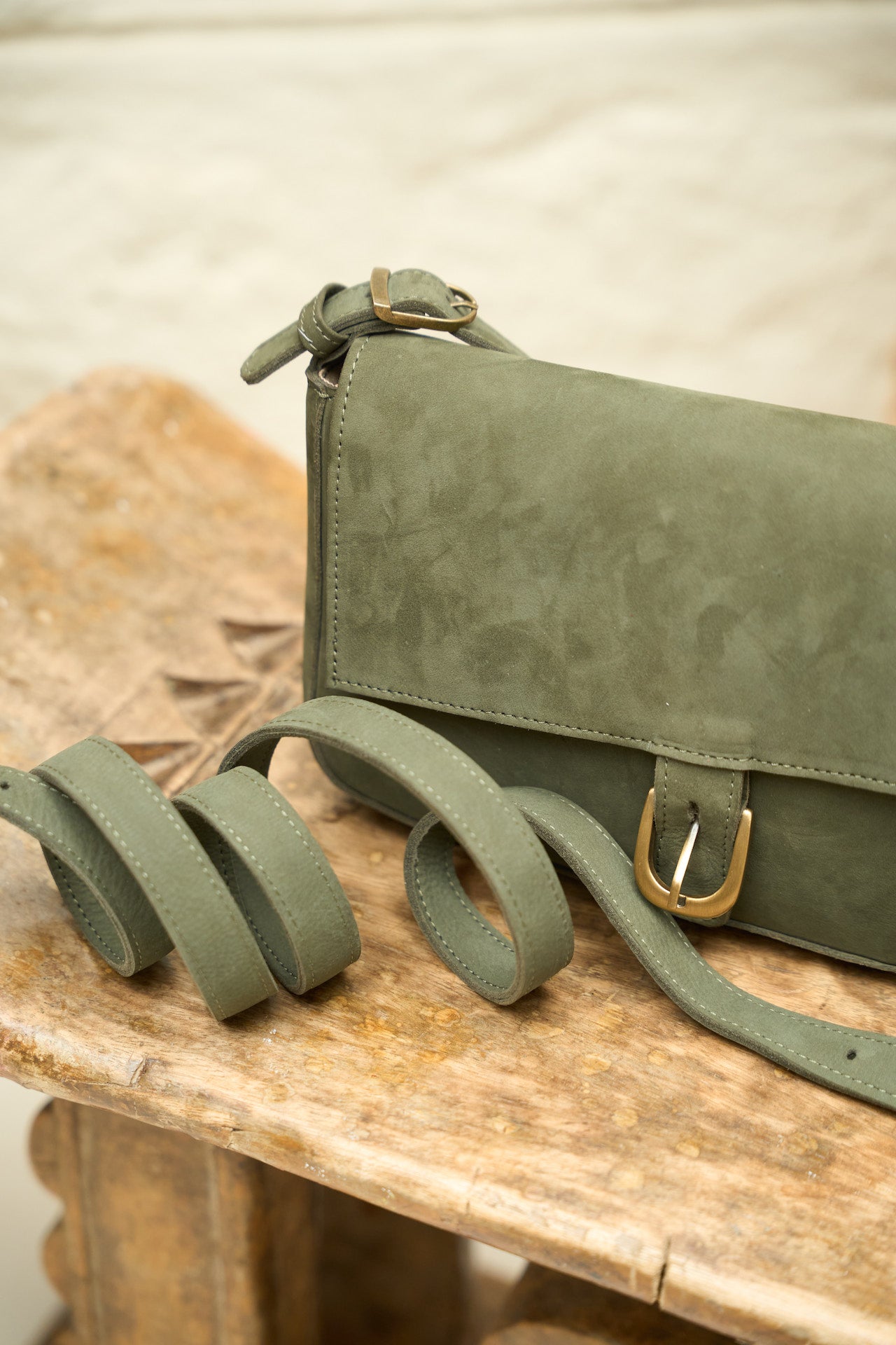 Green suede leather handbag with longer strap on a wooden surface