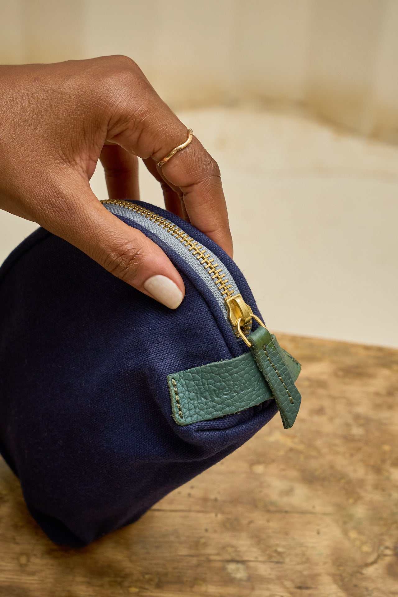 Navy blue pouch with green zipper held by a hand on a wooden surface