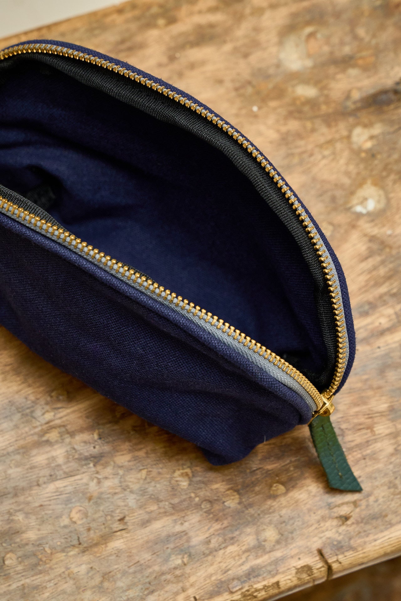 Navy travel pouch with gold zipper on a wooden surface