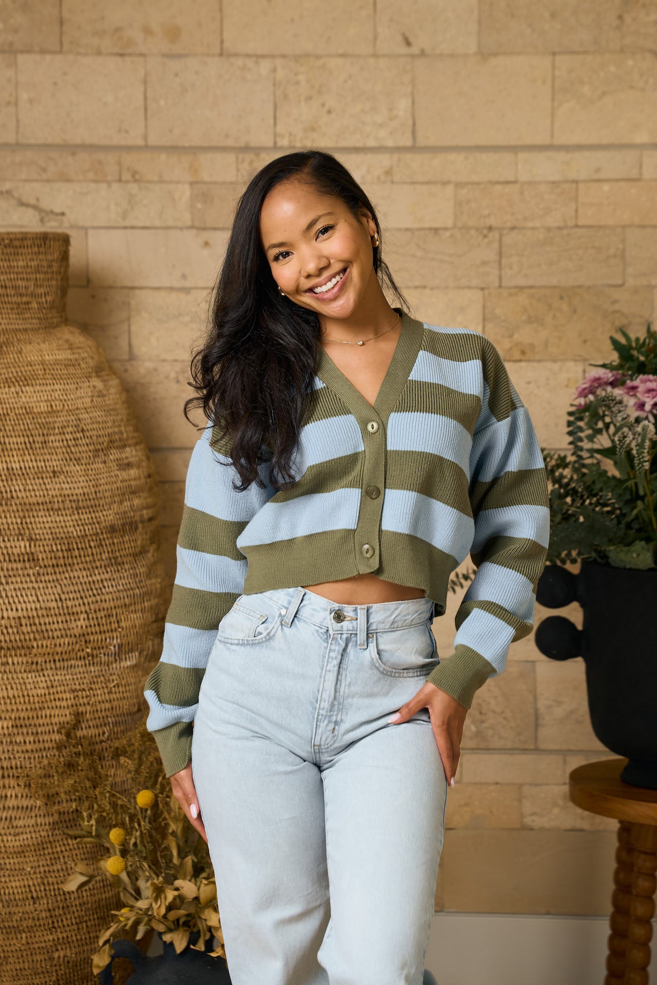 Woman wearing a Baby blue &sage striped sweater and jeans standing against a brick wall.