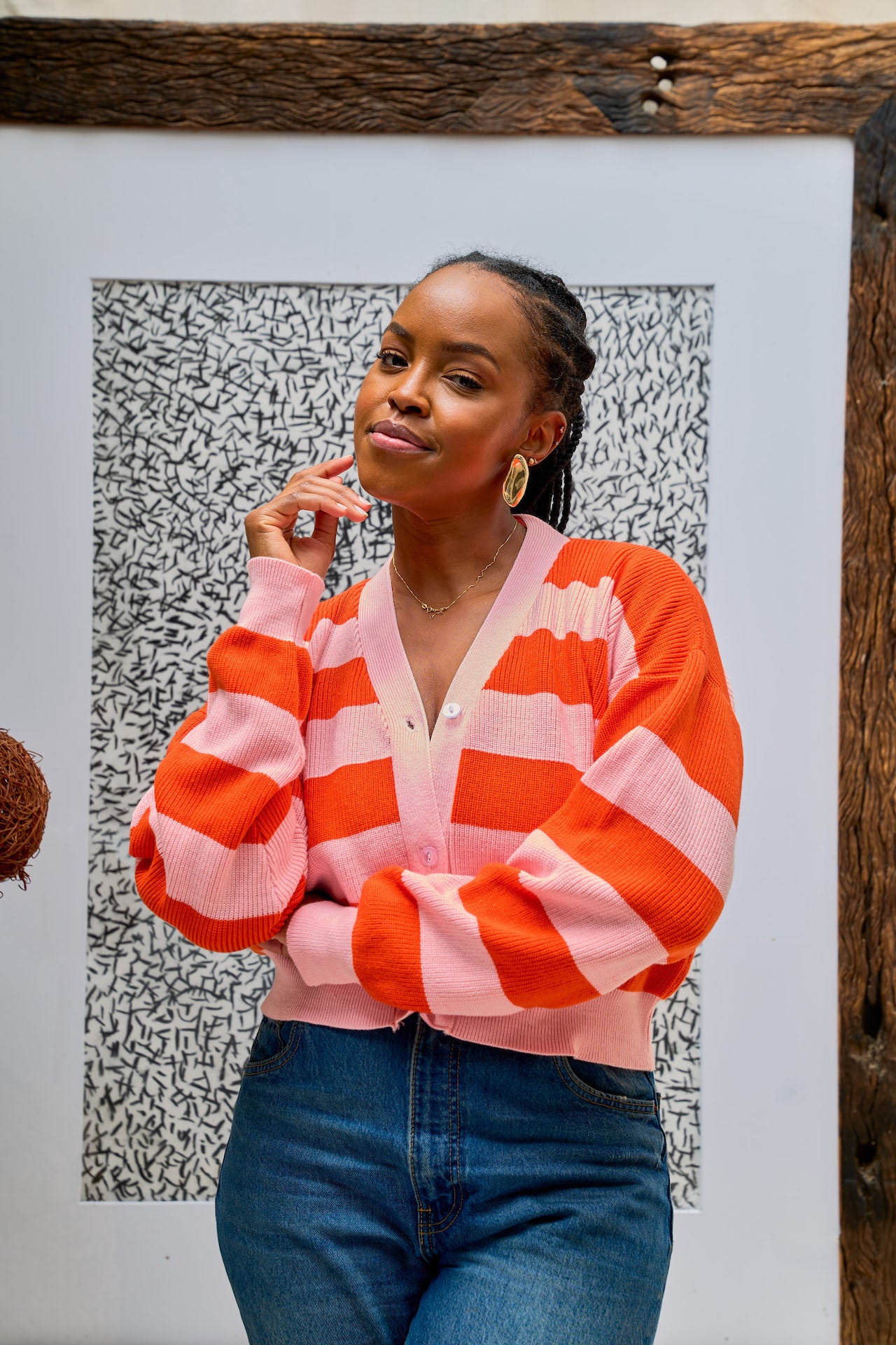 Woman wearing a pink and orange striped cropped cardigan styled with blue jeans.