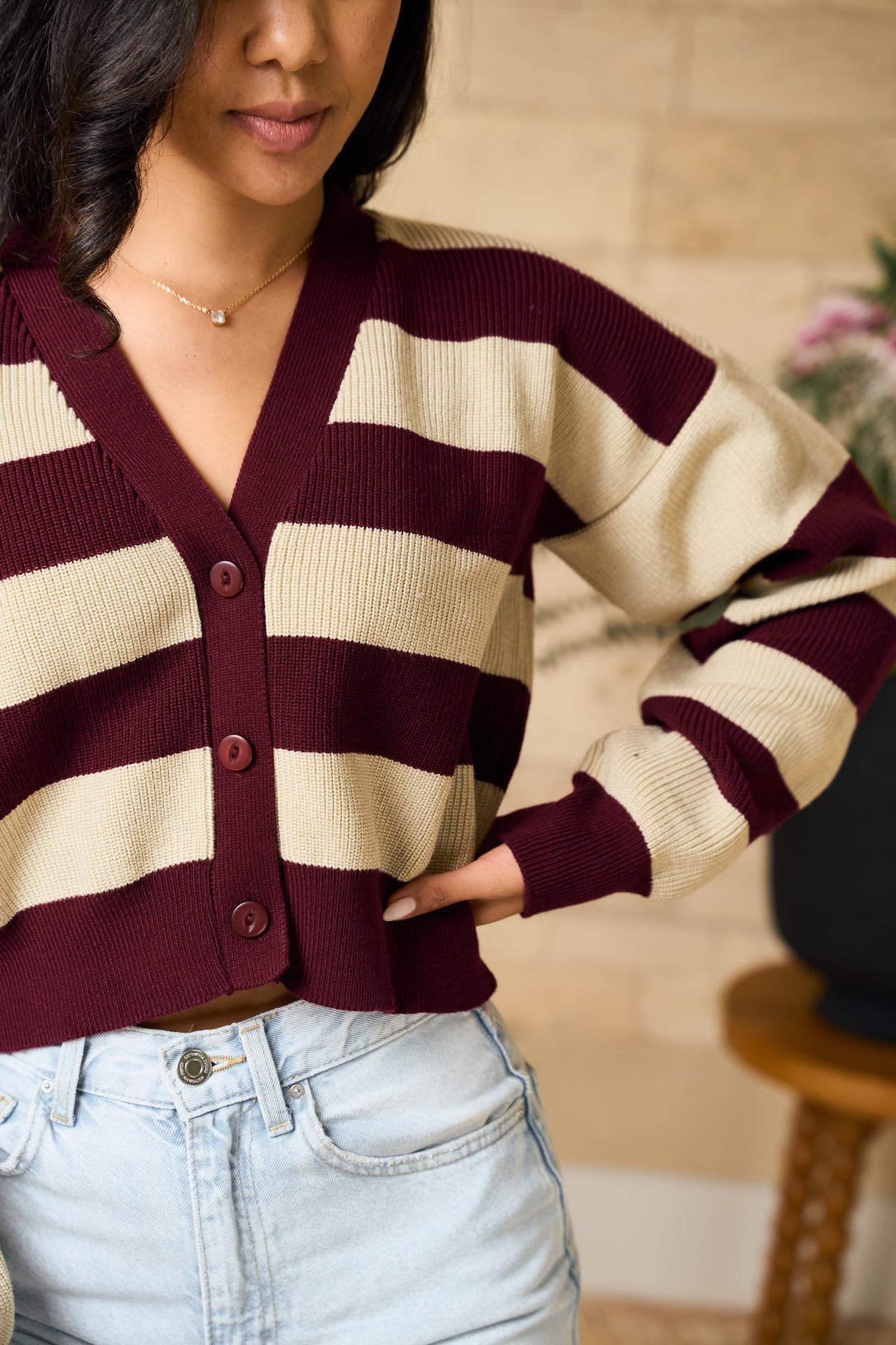 Model wearing a maroon and beige striped cropped  sweater with light blue jeans indoors.