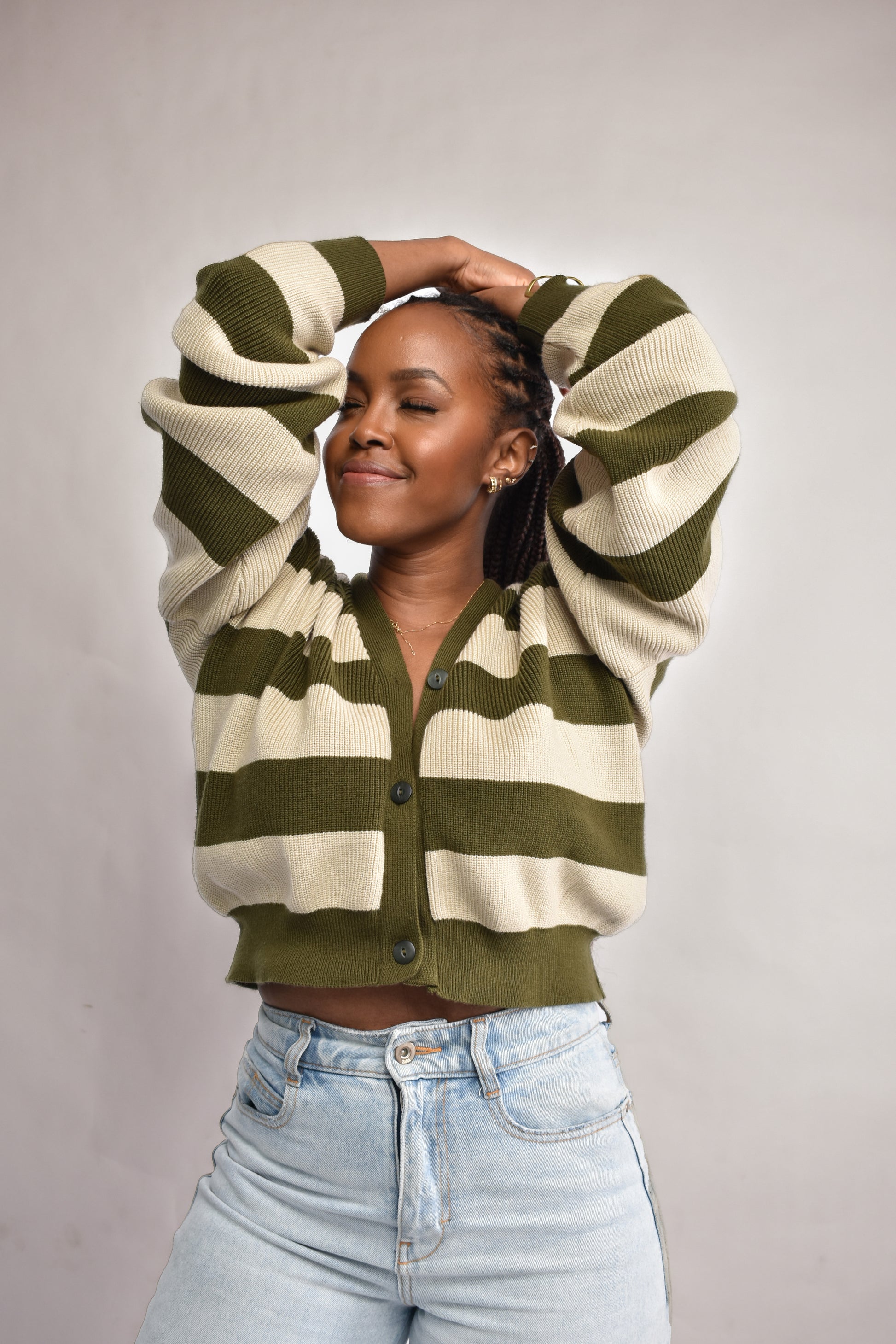 Woman wearing a green and beige striped cardigan with light blue jeans on a plain background