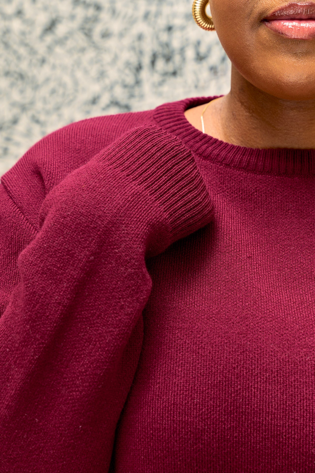 Close-up of a woman wearing a burgundy  shani crew neck sweater with a blurred background