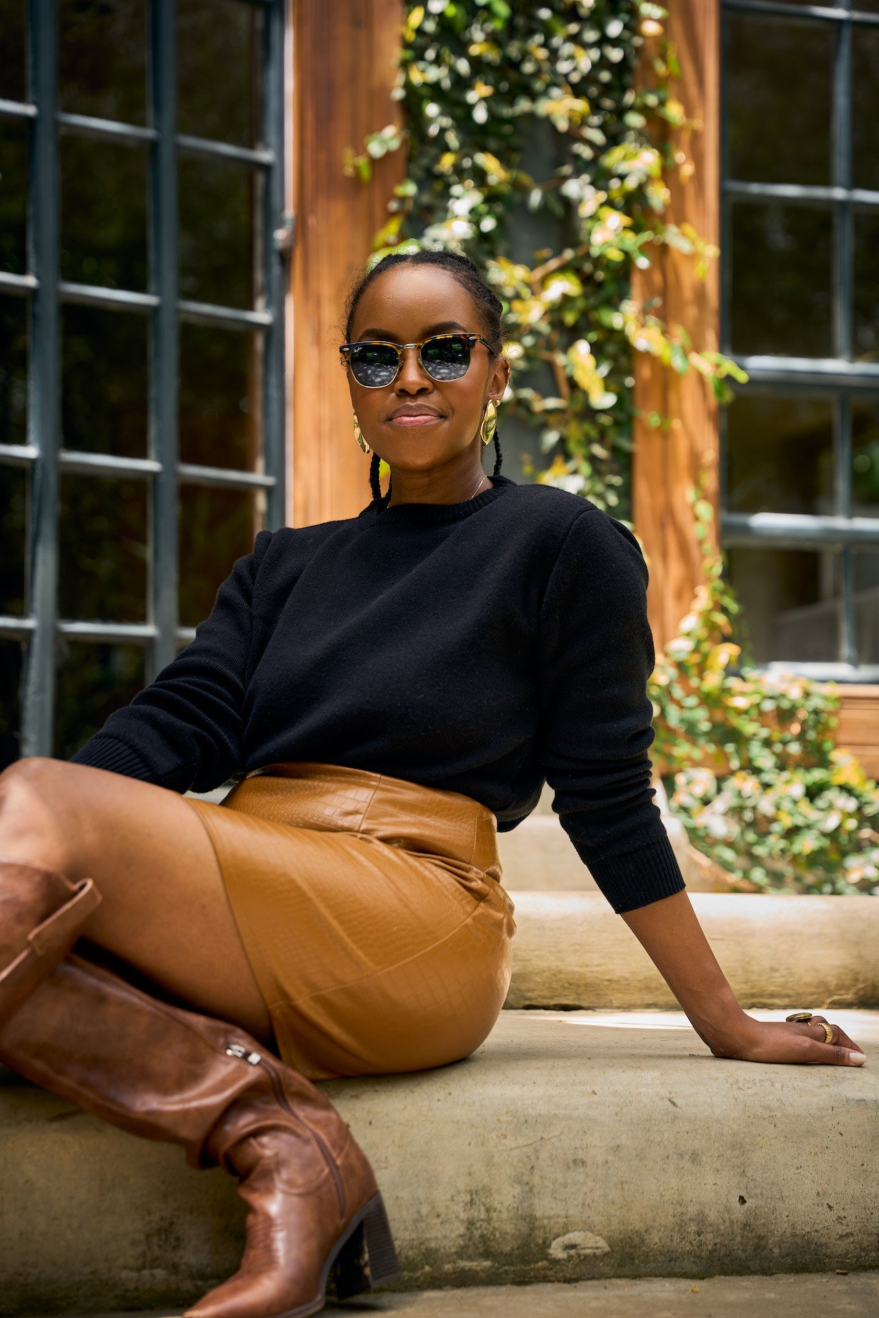 Woman wearing a black knit sweater   and brown leather skirt with sunglasses, sitting on steps.