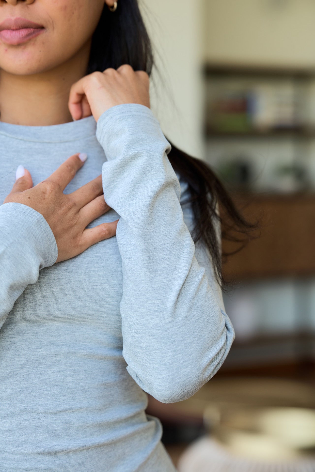 A close-up of a woman wearing a light gray long-sleeve crewneck tee, details of the sleeve.