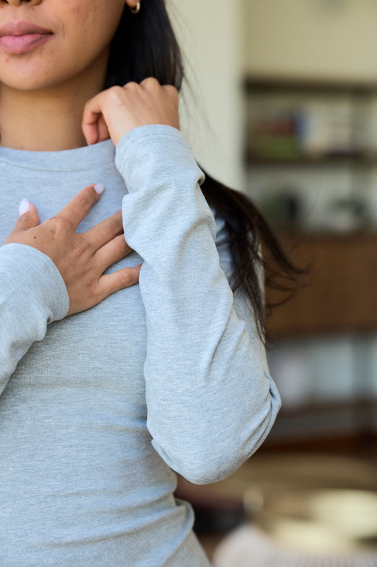 A close-up of a woman wearing a light gray long-sleeve crewneck tee, details of the sleeve.
