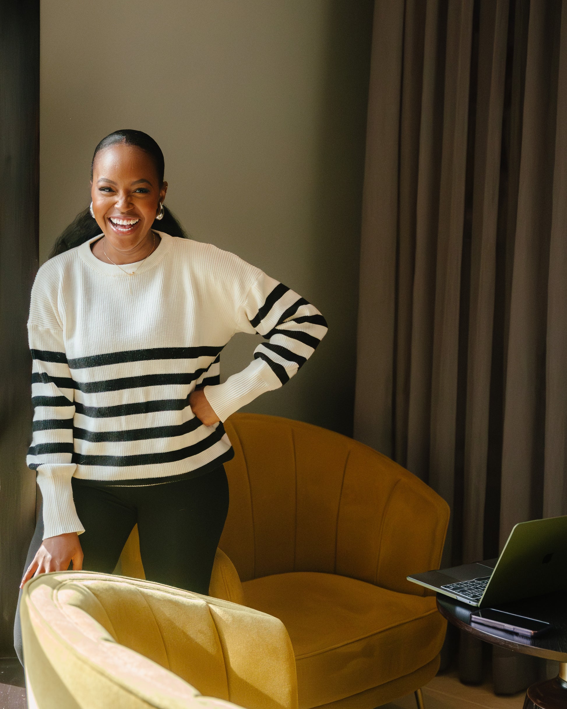 A woman  wearing the classic striped knit sweater in a Cream and black color combination, paired with black pants.