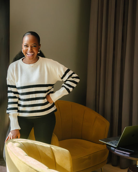 A woman  wearing the classic striped knit sweater in a Cream and black color combination, paired with black pants.