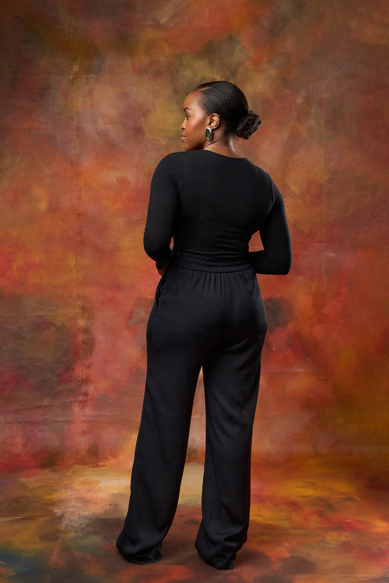 Back view of Woman wearing high-waisted Black wide leg pants from This Is Essential Kenya.
