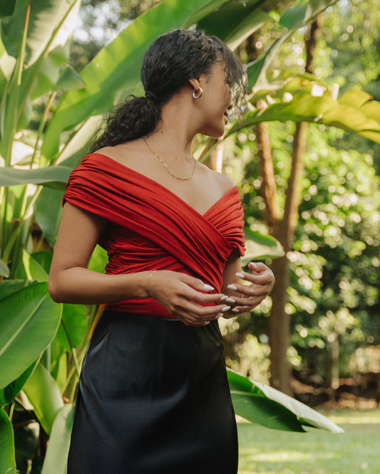 A woman wearing a red ruched bodysuit with a scoop neck, made of jersey stretch fabric, paired with a black satin skirt 