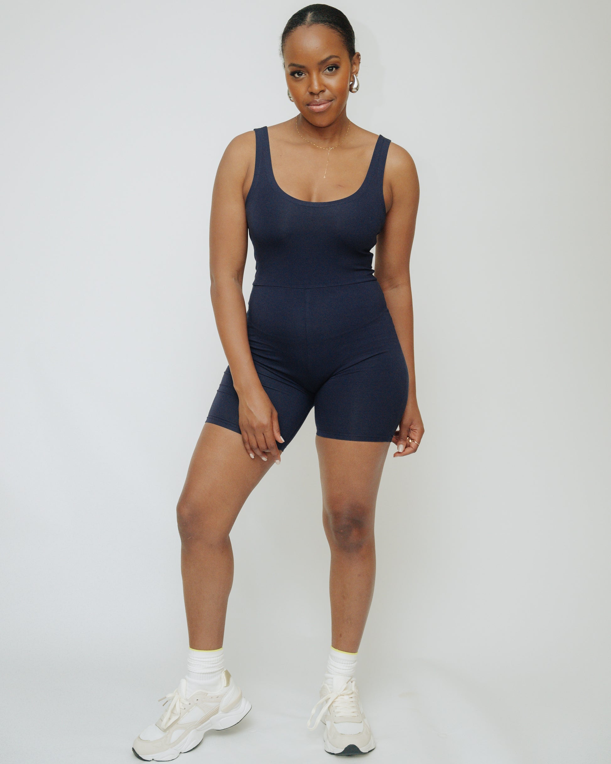 A person wearing a short unitard in navy color, with a scooped neckline and sleeveless.