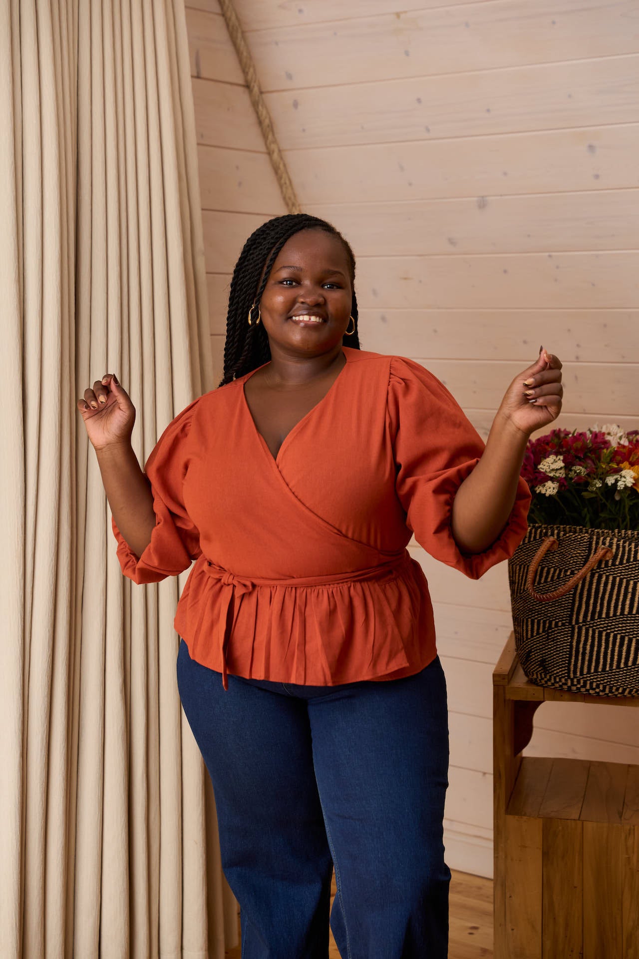 A smiling woman in the Yana Burnt Orange Linen Blend Wrap Top featuring a tied waist and V-neckline."
