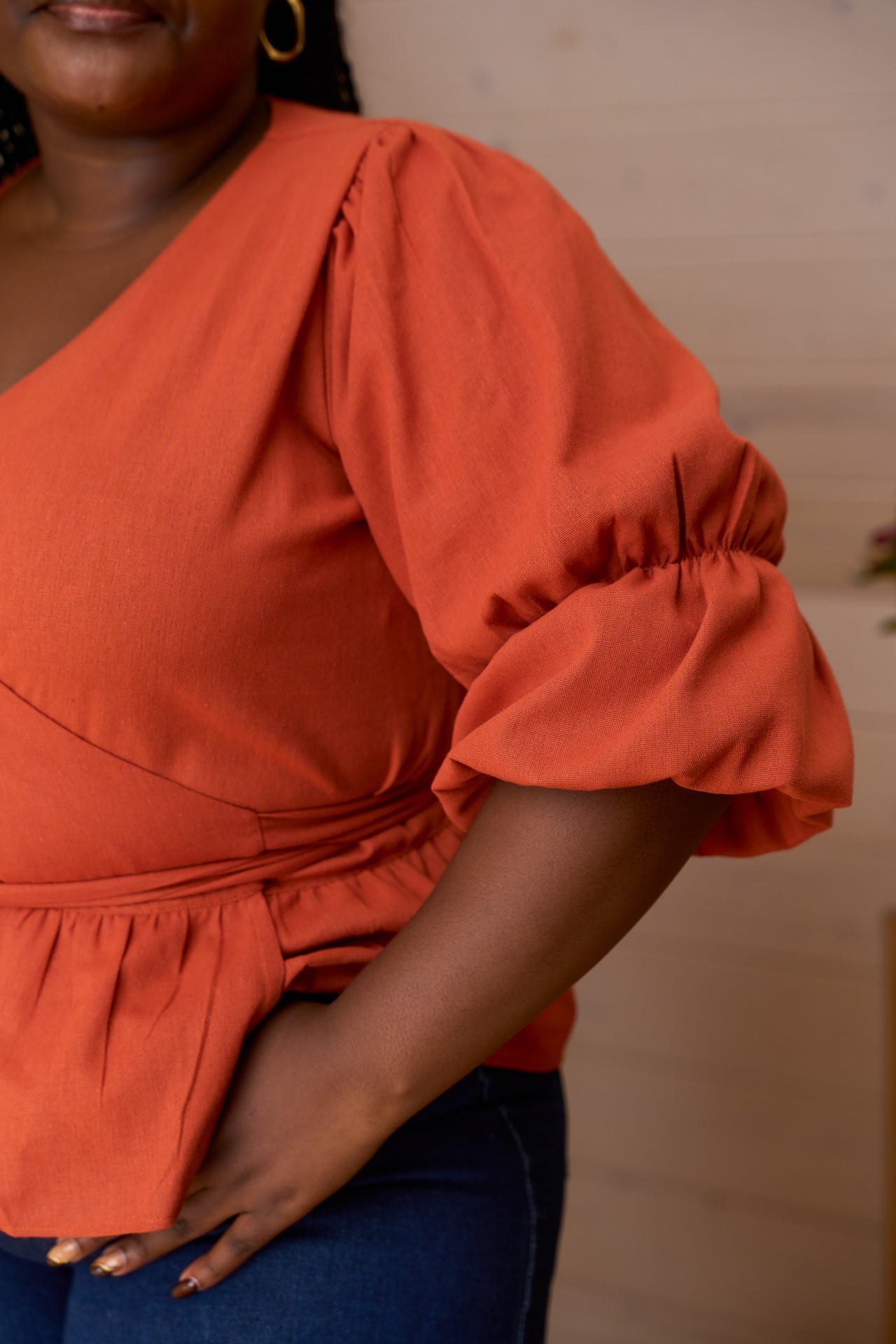 Woman wearing an orange Linen Top with ruffled sleeves against a neutral background