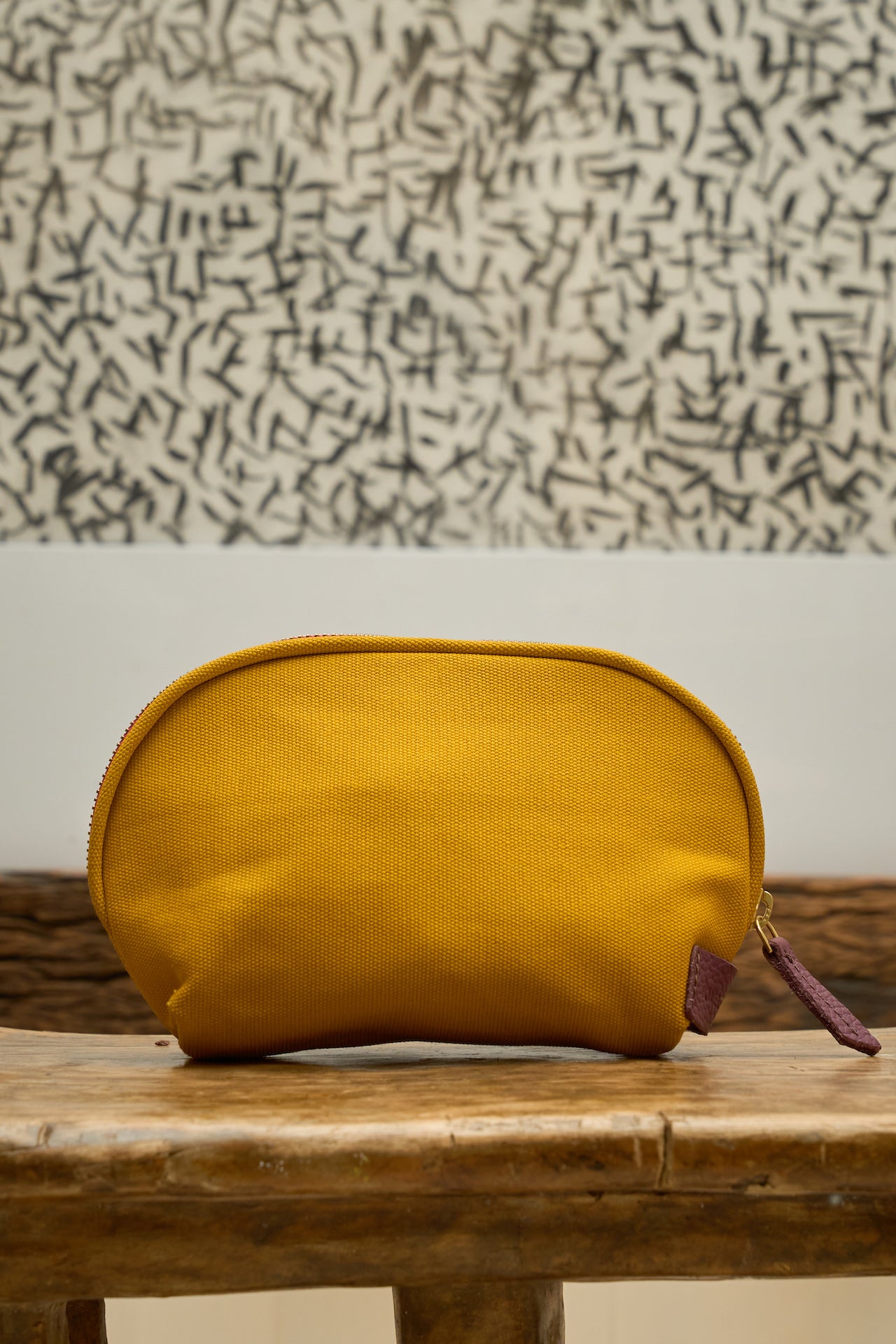 Yellow canvas pouch on a wooden surface with a patterned wall in the background.
